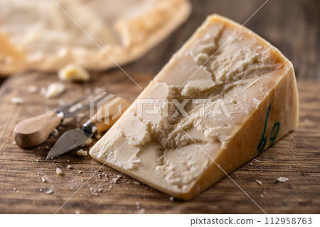 A block and pieces of Parmesan cheese on a cutting board along with a chisel and a skewer A block and pieces of Parmesan cheese on a cutting board along with a chisel and a skewer 112958763