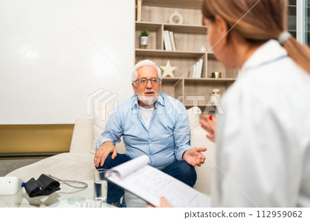 Female doctor examining older senior man in doctor office or at home. Old man patient and doctor have consultation in hospital room. Medicine healthcare medical checkup. Visit to doctor 112959062