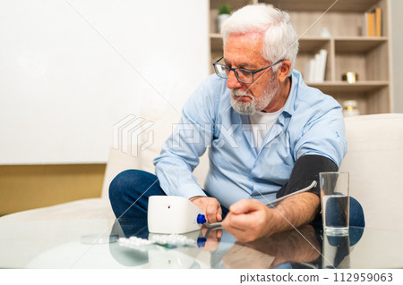 Hypertension problem in senior age. Old man measuring blood pressure with tonometer at home. Senior man have health problem making self checkup. Headache treatment of hypertension hypotension 112959063