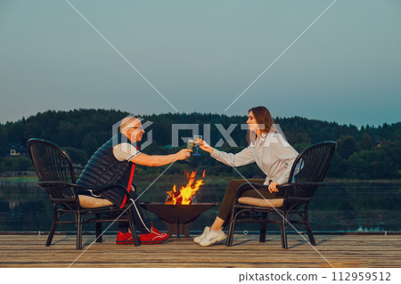 Couple celebrates the anniversary sitting on the pier by the fire 112959512