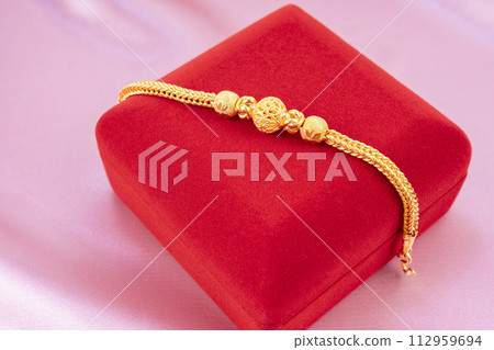 A gold bracelet and red velvet box on the red silk background display. 112959694