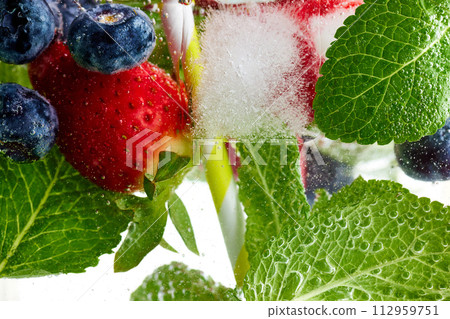 Close-up of fresh green mint leaves, strawberries and blueberries in water. Texture of cooling sweet summer's drink with macro bubbles. Lemonade. Close-up of fresh green mint leaves, strawberries and blueberries in water. Texture of cooling sweet summer's drink with macro bubbles. Lemonade. 112959751
