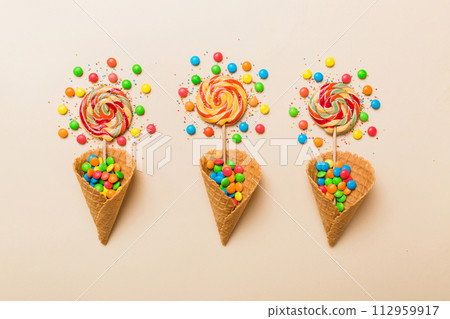 waffle cone full of assorted traditional candies falling out on colored background with copy space. Happy Holidays sale concept waffle cone full of assorted traditional candies falling out on colored background with copy space. Happy Holidays sale concept 112959917