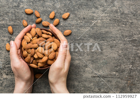 Woman hands holding a wooden bowl with almond nuts. Healthy food and snack. Vegetarian snacks of different nuts 112959927