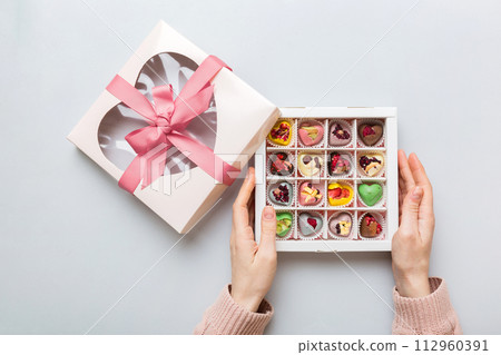 Female hands with delicious candies in box on color background 112960391