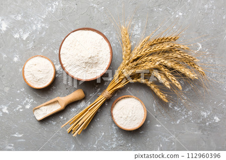 Flat lay of Wheat flour in wooden bowl with wheat spikelets on colored background. world wheat crisis Flat lay of Wheat flour in wooden bowl with wheat spikelets on colored background. world wheat crisis 112960396