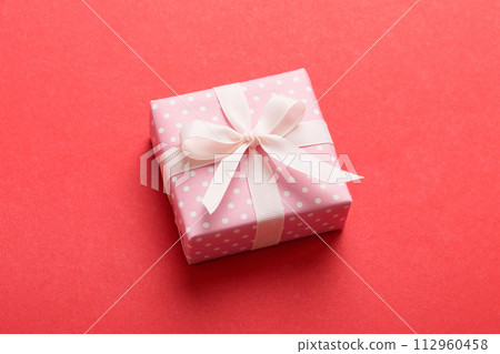wrapped Christmas or other holiday handmade gift box in color paper with ribbon on colored background. Present box, decoration of gift on colored table, top view with copy space 112960458