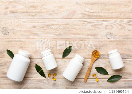 Omega-3 capsules lie in white bottle on a table with green leaves background. Fish oil tablets. Biologically active additives. omega 6, omega 9, vitamin A, E, D, vitamin D3 top view with copy space 112960464