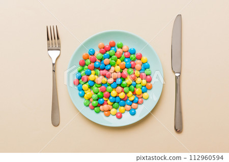 cutlery on table and sweet plate of candy. Health and obesity concept, top view on colored background 112960594
