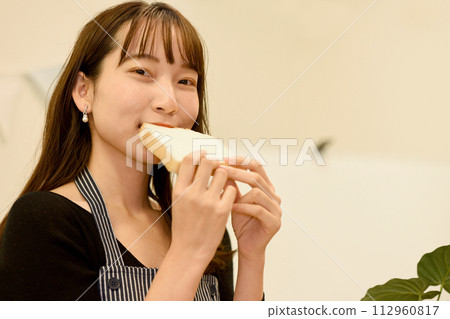 Smiling young Asian woman eating bread 112960817