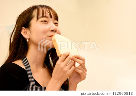 Smiling young Asian woman eating bread 112960818