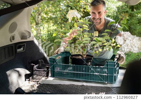 Happy Man Loading Potted Flowers into Car Trunk in Summer Happy Man Loading Potted Flowers into Car Trunk in Summer 112960827