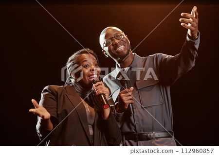 Waist up portrait of two African American performers on stage speaking to audience with spotlight 112960857