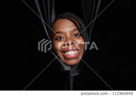 Close up of smiling African American woman peeking from curtains on theater stage and looking at camera Close up of smiling African American woman peeking from curtains on theater stage and looking at camera 112960949