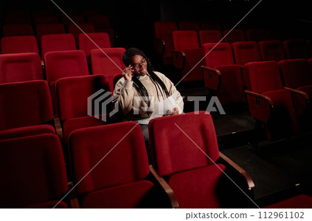 Minimal portrait of smiling African American woman reading lines while sitting in empty audience at theater copy space Minimal portrait of smiling African American woman reading lines while sitting in empty audience at theater copy space 112961102