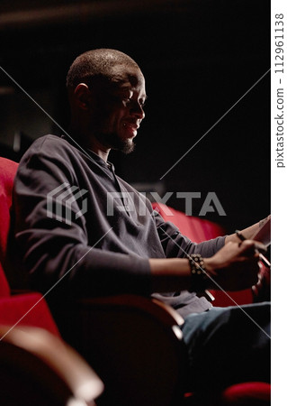 Vertical portrait of African American man sitting in audience in low light and reading script Vertical portrait of African American man sitting in audience in low light and reading script 112961138