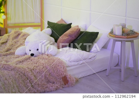 Modern interior design of bedroom with orthopedic, comfortable mattress, green, white, brown pillows, brown soft fluffy blanket, white teddy bear, white table with candles. Background with copy space. 112962194