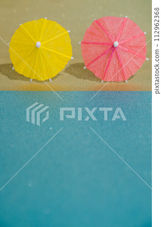 Abstract beach with glitter paper sand and water and cocktail umbrellas. Summer aesthetic mockup template background on a tropical beach holiday Abstract beach with glitter paper sand and water and cocktail umbrellas. Summer aesthetic mockup template background on a tropical beach holiday 112962368