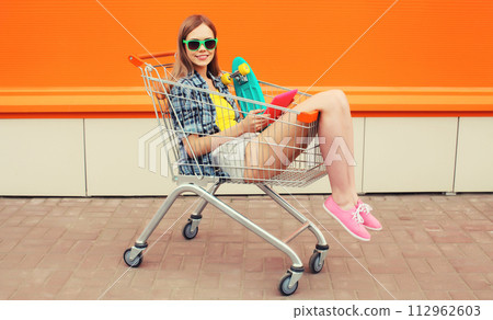 Modern stylish young woman using digital tablet computer in shopping trolley cart on city street Modern stylish young woman using digital tablet computer in shopping trolley cart on city street 112962603