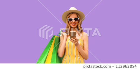 Beautiful happy young woman looking at phone with colorful shopping bag on purple studio background 112962854
