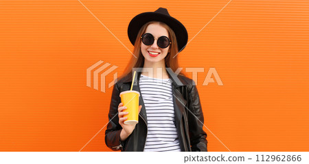 Portrait stylish young woman drinking juice posing in black rock style leather jacket, round hat 112962866