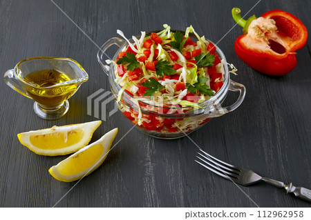 Vegetarian vegetable salad of chopped cabbage and bell peppers dressed with olive oil and lemon in a glass bowl on a black wooden table 112962958
