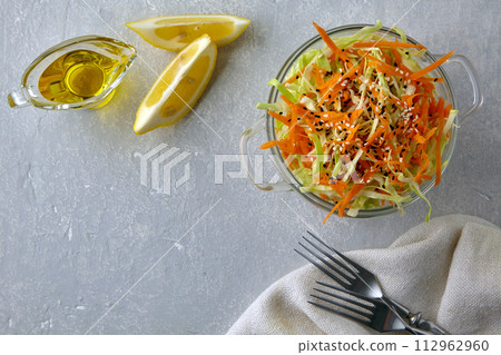 Vegetarian vegetable salad of chopped cabbage and carrots dressed with olive oil and lemon, with sesame seeds in a glass bowl on a modest stone table 112962960