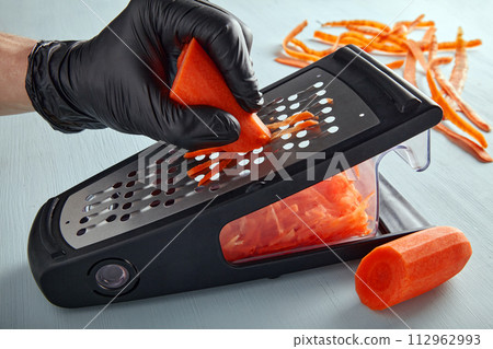 Cook in black latex gloves shreds carrots on a metal grater 112962993