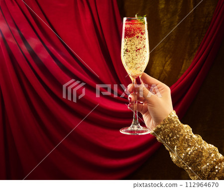 Woman's hand in festive clothes holding glass of sparkle wine decorated with strawberry. against vintage background. 112964670