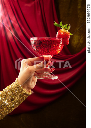 Unrecognizable woman holding glass of sweet and sour cocktail decorated with strawberry at restaurant with vintage. 112964676