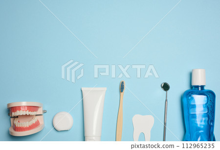 Mouthwash, toothpaste tube, dental floss and medical mirror on a blue background, oral hygiene. 112965235