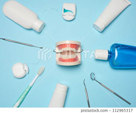 Mouthwash, toothpaste tube, dental floss and medical mirror on a blue background, oral hygiene. Mouthwash, toothpaste tube, dental floss and medical mirror on a blue background, oral hygiene. 112965317