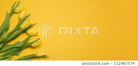 Bouquet of blooming yellow tulips with green leaves on a yellow background, top view 112965574