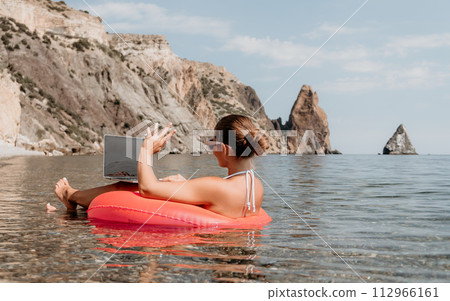 Woman freelancer works on laptop swimming in sea on pink inflatable ring. Happy tourist in sunglasses floating on inflatable donut and working on laptop computer in calm ocean. Remote working anywhere Woman freelancer works on laptop swimming in sea on pink inflatable ring. Happy tourist in sunglasses floating on inflatable donut and working on laptop computer in calm ocean. Remote working anywhere 112966161