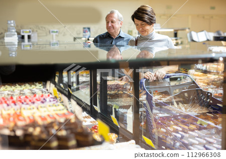 Female customer chooses sweet cakes with interest of the grocery department of supermarket Female customer chooses sweet cakes with interest of the grocery department of supermarket 112966308