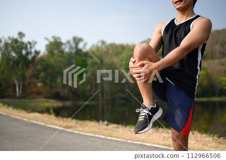 Sporty man doing stretching exercises preparing for morning workout in the park Sporty man doing stretching exercises preparing for morning workout in the park 112966506