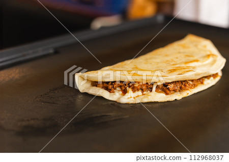 Preparing fresh quesadilla on black grill at local food market. 112968037