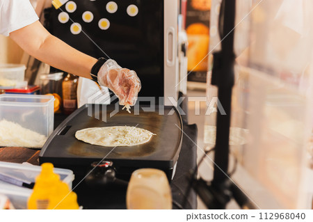 Chef sprinkles a tortilla with cheese preparing fresh quesadilla on black grill. Chef sprinkles a tortilla with cheese preparing fresh quesadilla on black grill. 112968040