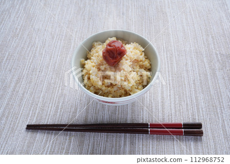 A Japanese breakfast consisting of freshly cooked, piping hot brown rice topped with pickled plums and coarse food. 112968752
