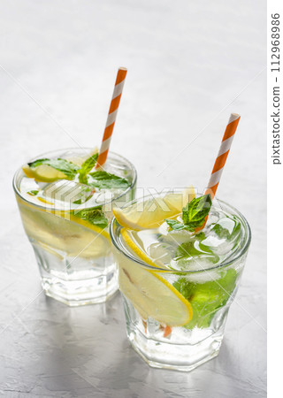 Two glasses of lemonade adorned with ice, lemon slices, and fresh mint leaves, evoking a refreshing summer vibe. Highlighting cooling drinks and seasonal enjoyment. 112968986