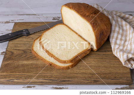 Wheat (white) bread with a crispy crust on a wooden board, cut into slices. Homemade baking in rustic style. Selective focus, close-up. Wheat (white) bread with a crispy crust on a wooden board, cut into slices. Homemade baking in rustic style. Selective focus, close-up. 112969166