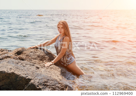 Woman summer travel sea. Happy tourist enjoy taking picture outdoors for memories. Woman traveler posing on the beach at sea surrounded by volcanic mountains, sharing travel adventure journey 112969400