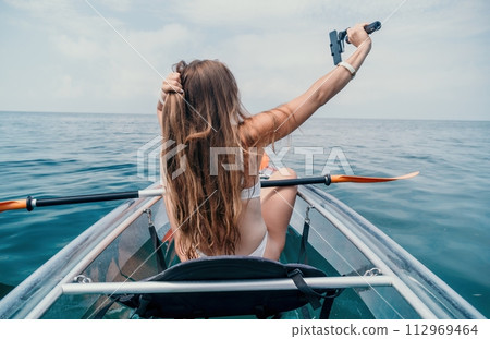 Woman in kayak back view. Happy young woman with long hair floating in transparent kayak on the crystal clear sea. Summer holiday vacation and cheerful female people relaxing having fun on the boat 112969464