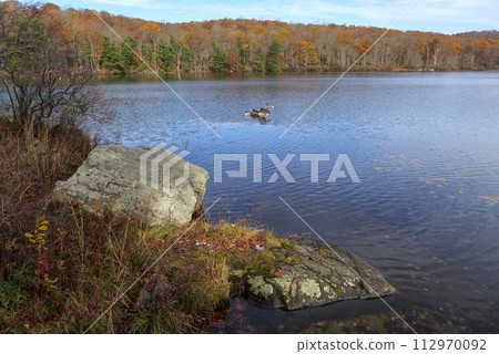 Autumn lake reflecting on a blue sky background and forest landscape 112970092
