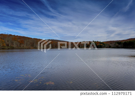 Autumn lake reflecting on a blue sky background and forest landscape 112970171