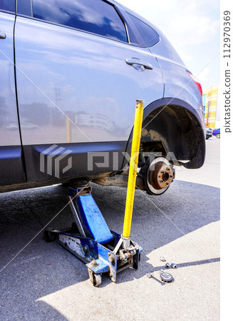 Wheels replacement. Lifting car and changing wheels using trolley jack Wheels replacement. Lifting car and changing wheels using trolley jack 112970369