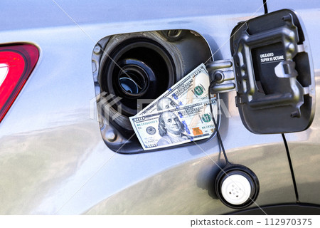 American dollars bills in the gas tank of a vehicle. Concept photo of the rising fuel price American dollars bills in the gas tank of a vehicle. Concept photo of the rising fuel price 112970375