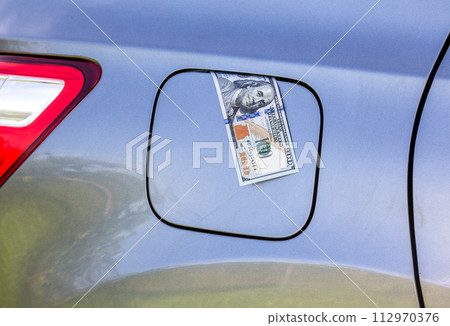 American dollars bills in the gas tank of a vehicle. Concept photo of the rising fuel price American dollars bills in the gas tank of a vehicle. Concept photo of the rising fuel price 112970376
