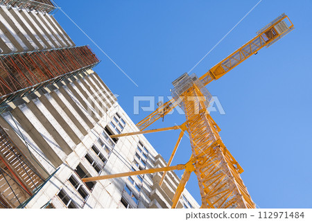 Crane and building under construction against blue sky. Construction work site. Crane and building under construction against blue sky. Construction work site. 112971484