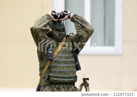 A Russian military man looks at the sky through binoculars. Tracking unmanned aerial vehicles. 112971525